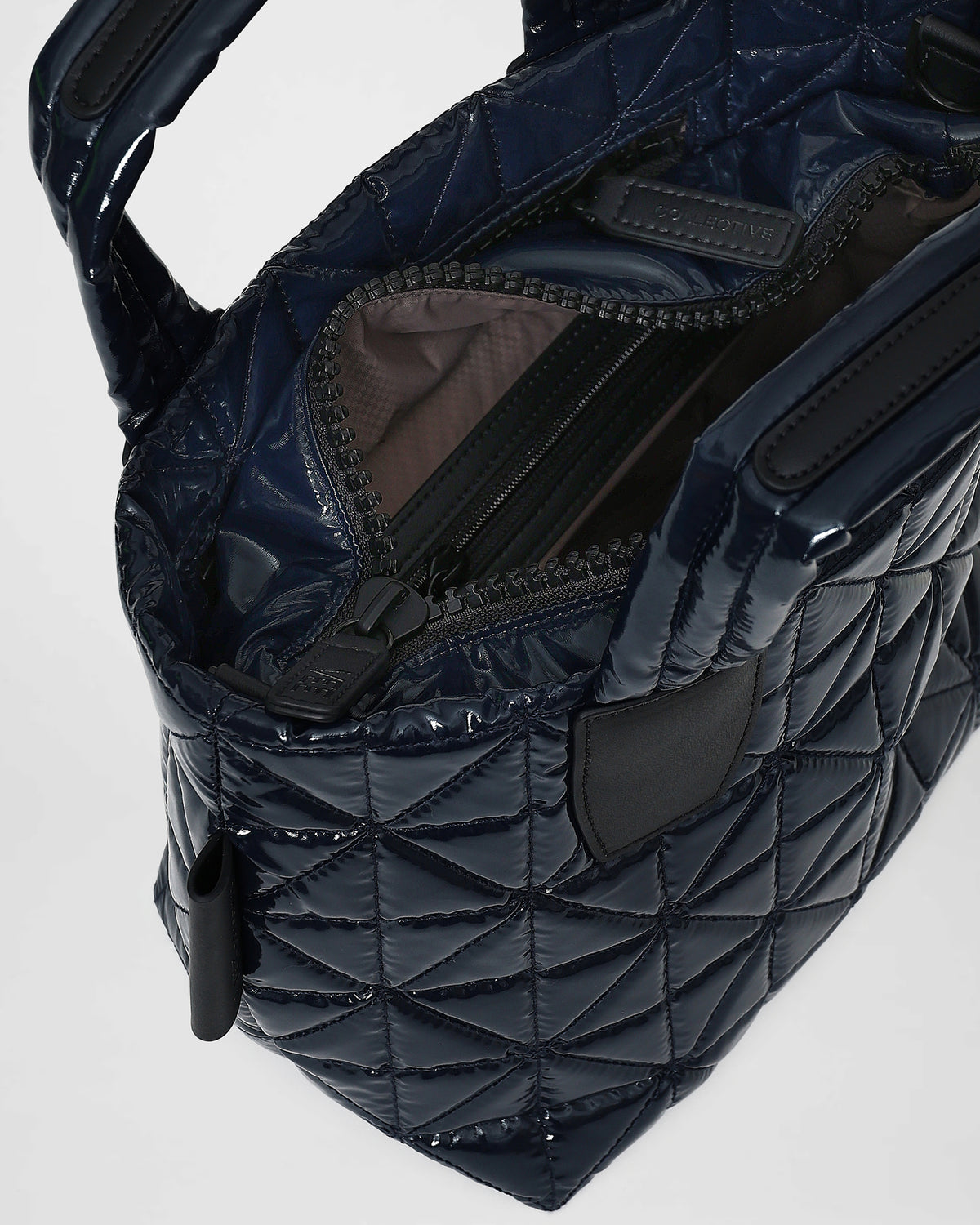 The image shows an open Vee tote bag with a quilted triangle design in a deep midnight blue color. The interior features a zippered compartment and a smooth lining, showcasing the bags modern, versatile style.
