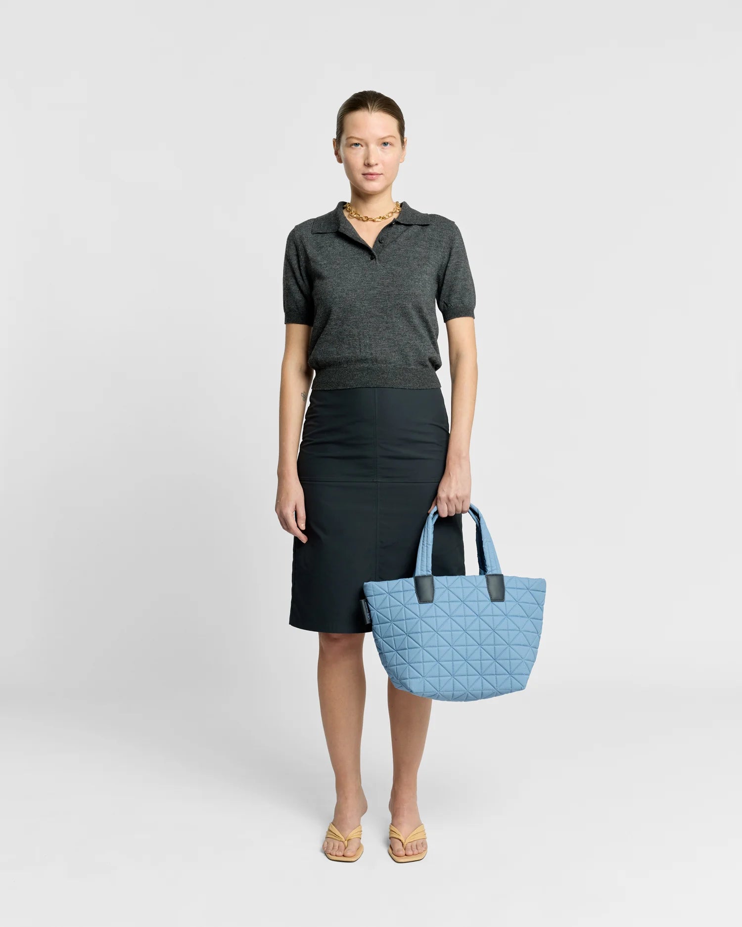 On-body picture of a woman holding the Small Vee Tote Bag in Pigeon Blue by Vee Collective, wearing a minimalistic outfit against a clean studio background.