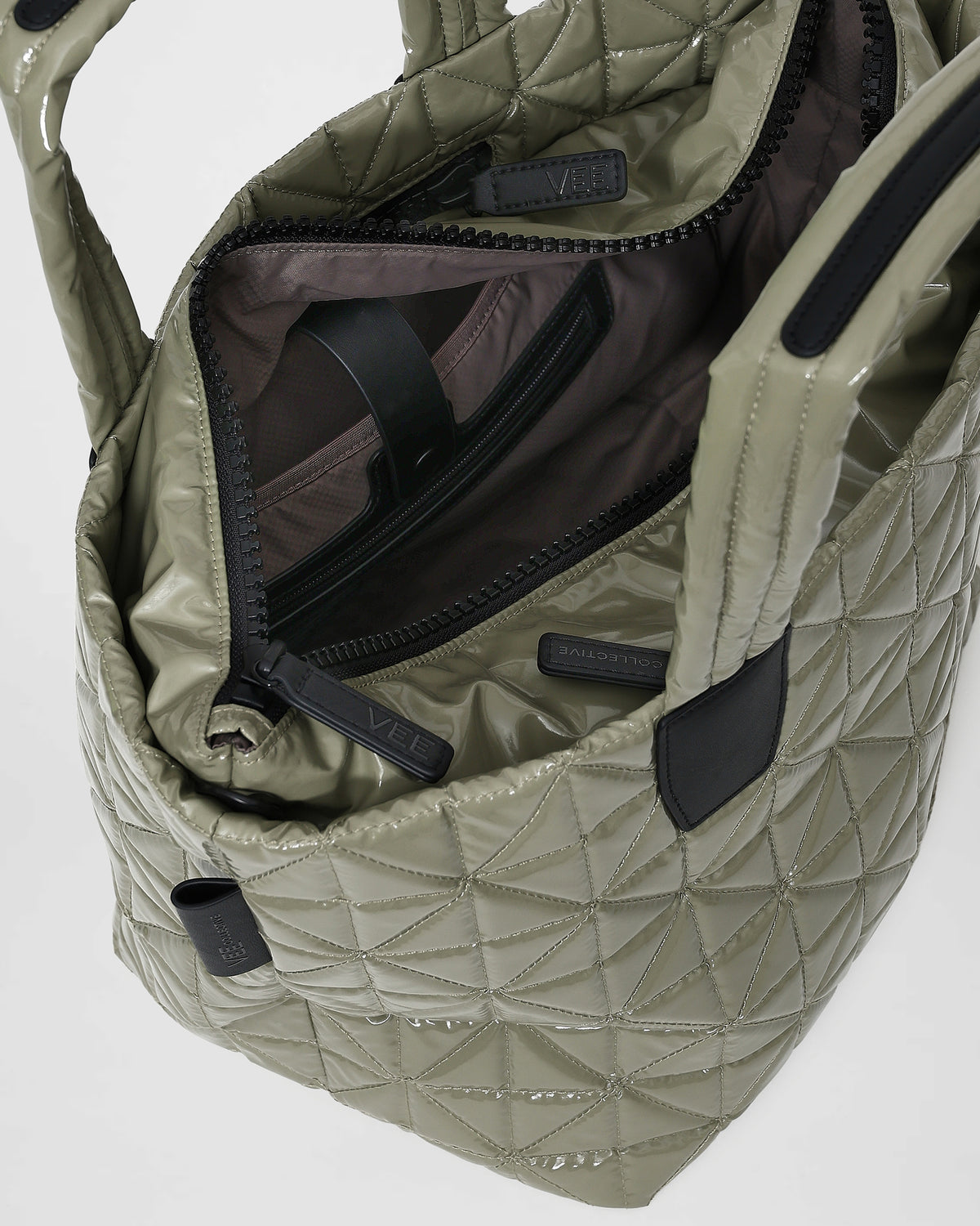 An open Vee tote bag showcases its quilted triangle design with geometric stitching. The interior features a dark lining with compartments, including a zippered pocket, ideal for organizing essentials.