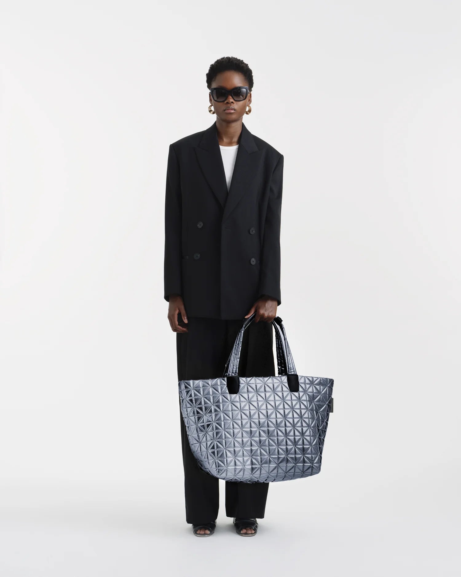 On-body picture of a woman holding the Vee Weekender Tote Bag in Icy Silver by Vee Collective, wearing a minimalistic outfit against a clean studio background.