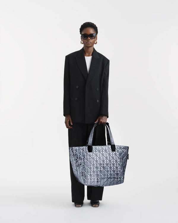 On-body picture of a woman holding the Vee Weekender Tote Bag in Icy Silver by Vee Collective, wearing a minimalistic outfit against a clean studio background.