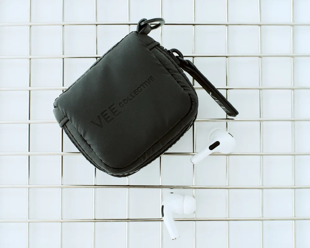 Porter Pods Case in matt black lying in a metallic basket with a pair of AirPods.