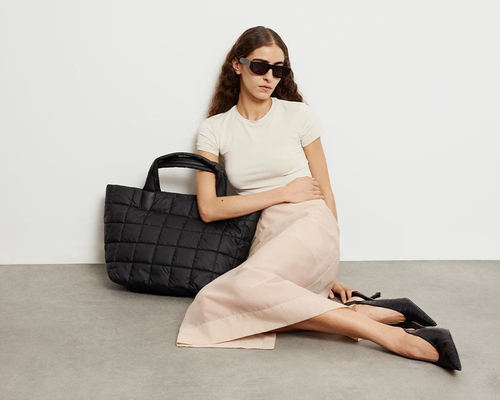 Porter Tote Medium tote bag  by Vee Collective in matt black resting next to a seated model.