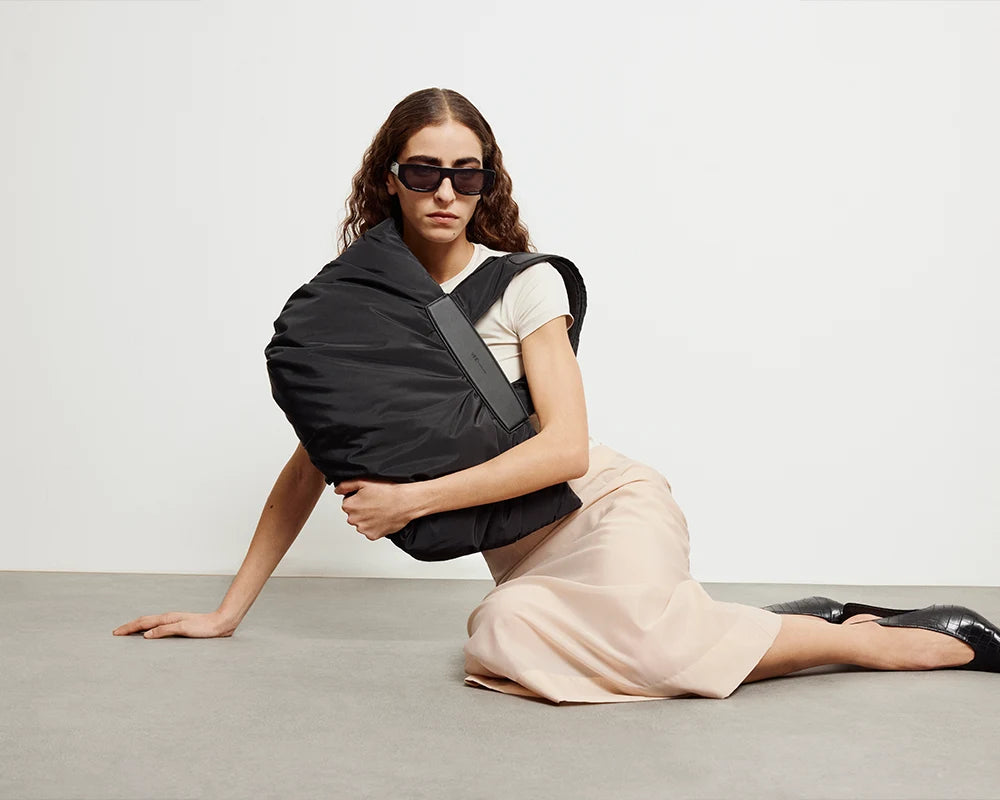 Black Caba Tote bag in Medium by Vee Collective showcased by a seated model in neutral-toned clothing.