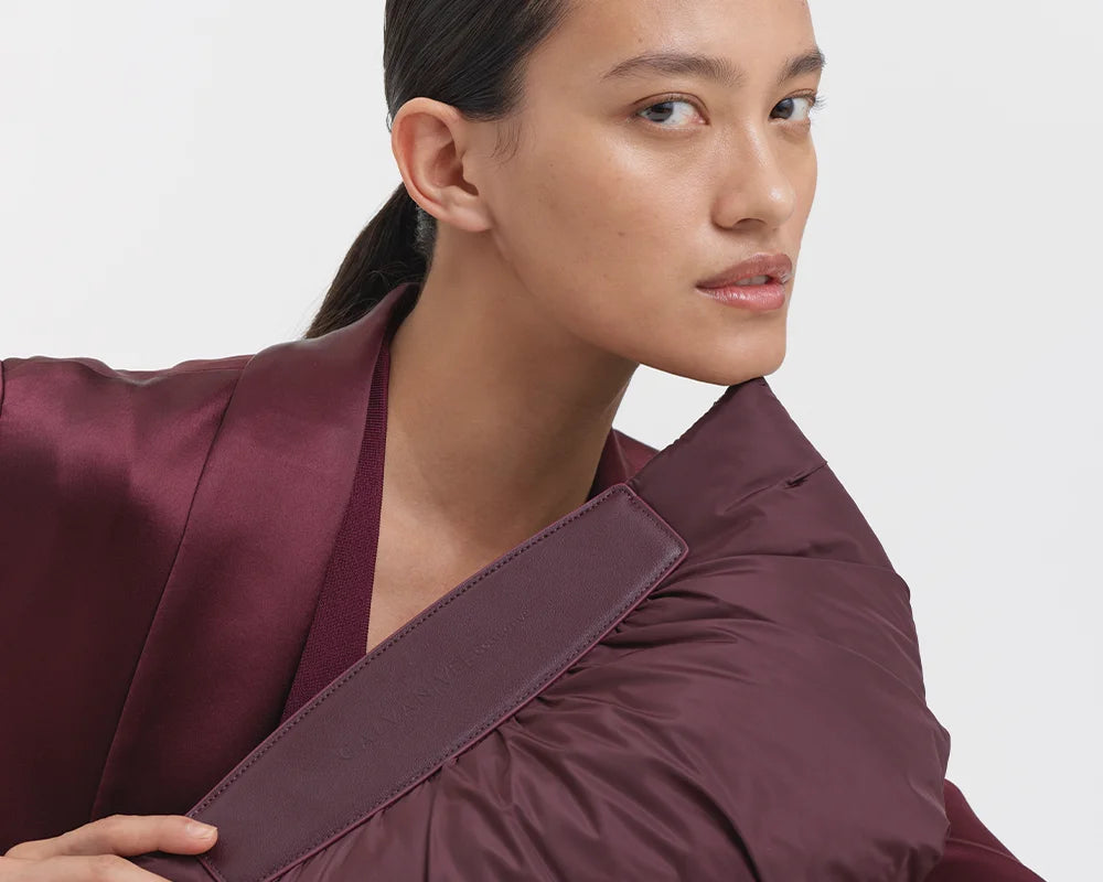 Close-up of a woman wearing a mahogany suit, holding the Galvan x Vee Collective Caba Clutch in mahogany in one hand in front of her upper body, up to her chin.