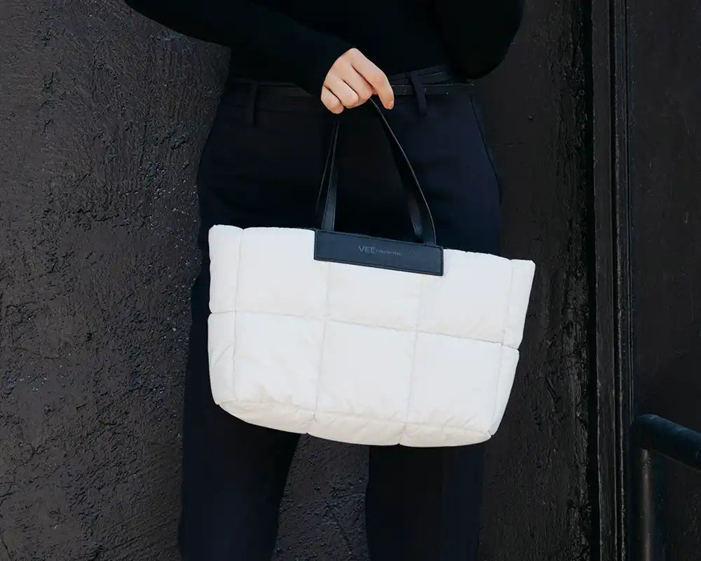 White quilted handbag held by a person against a dark background